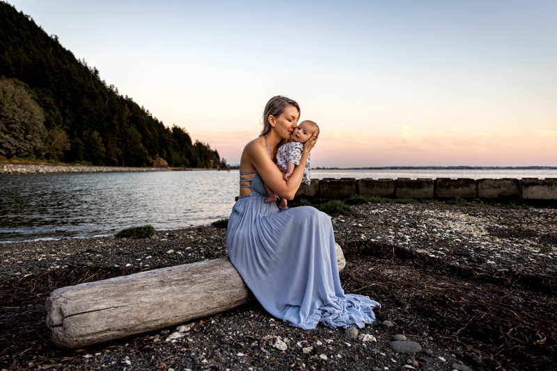 Family Photography, Woman in blue dress sitting on a log holding baby kissing its cheek